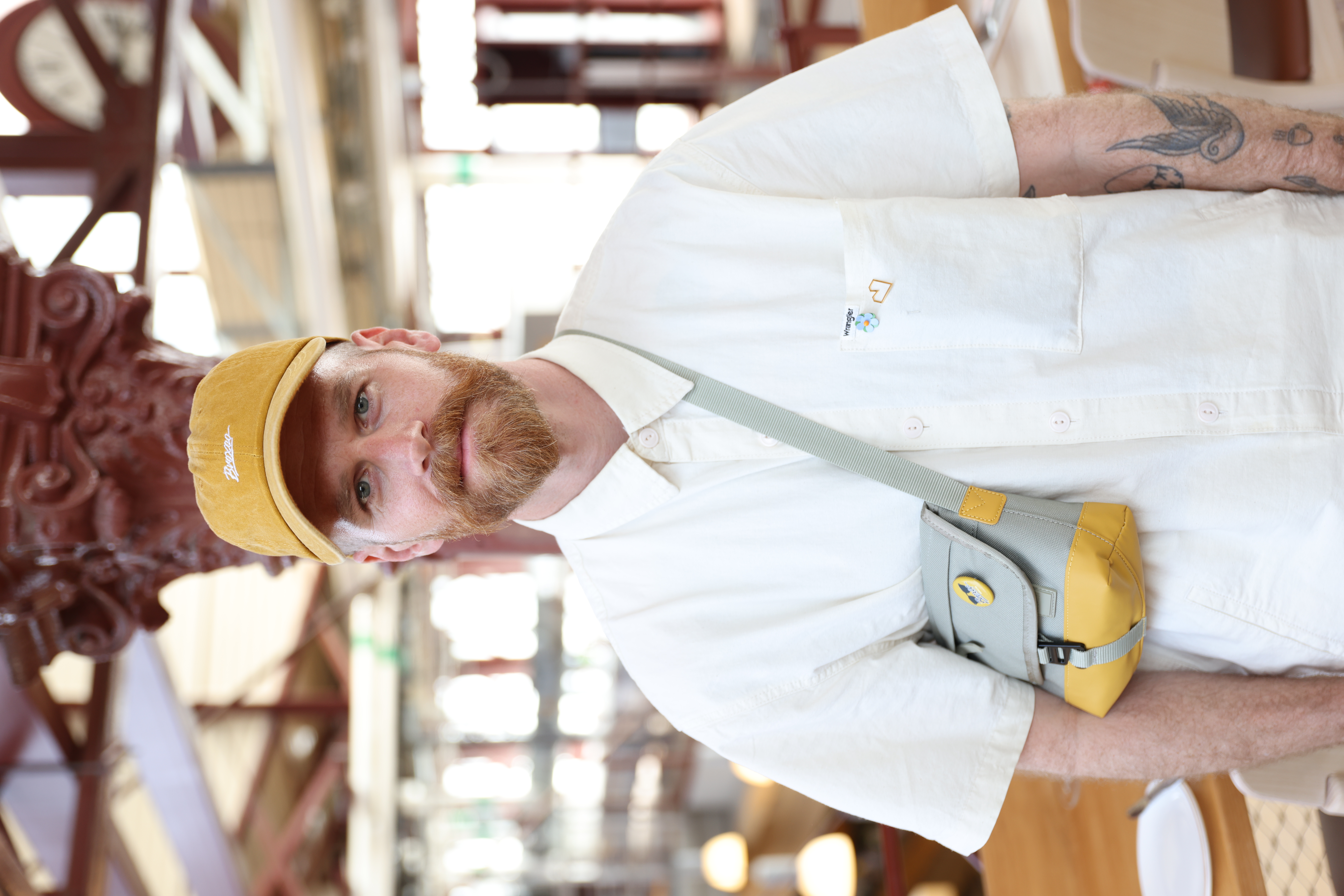 Porträtt på Niclas. Han bär en vit skjorta, senapsgul keps och har ett rödaktigt skägg.