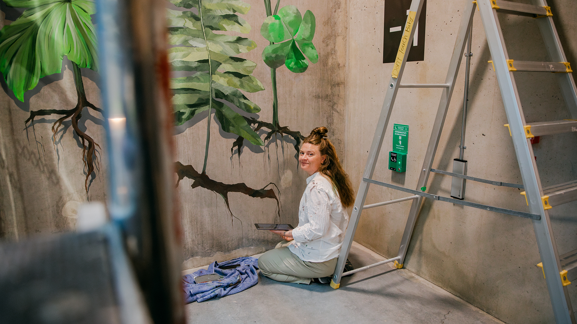 Konstnären Malin Sparrvardt sitter på golvet vid sin målning